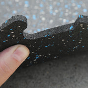 Close-up of a side view of a blue/gray rubber gym tile held by a thumb against a blurred background