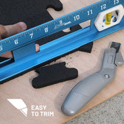 Hand holding a straight edge next to a box cutter showing one of the rubber gym tile tabs having been cut off.