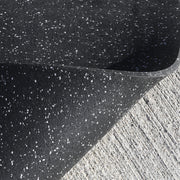 Close-up of a black rubber mat with white specks on a concrete floor.
