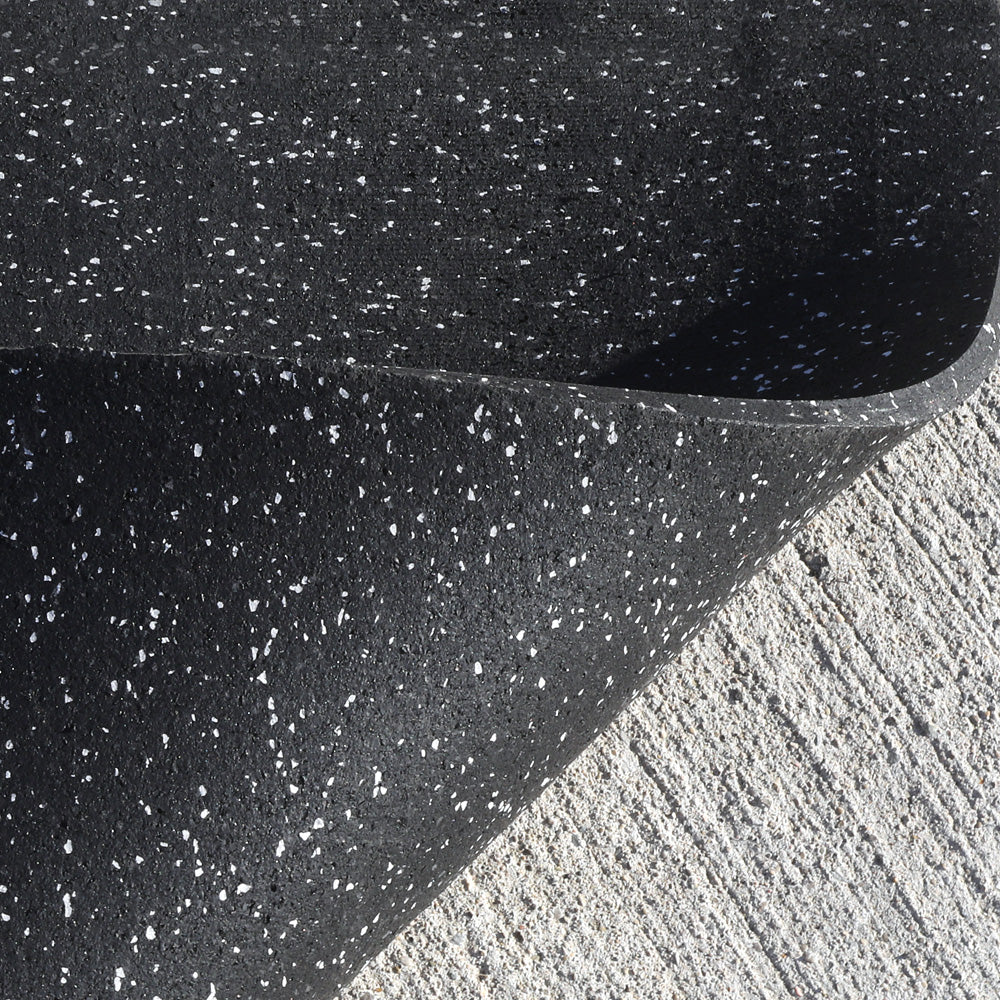 Close-up of a black rubber mat with white specks on a concrete floor.