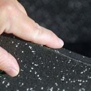 Hand holding a black rubber mat with gray speckles against a blurred background