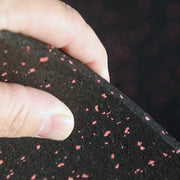 Close-up of a hand holding black rubber gym mat with red specks against a blurred background
