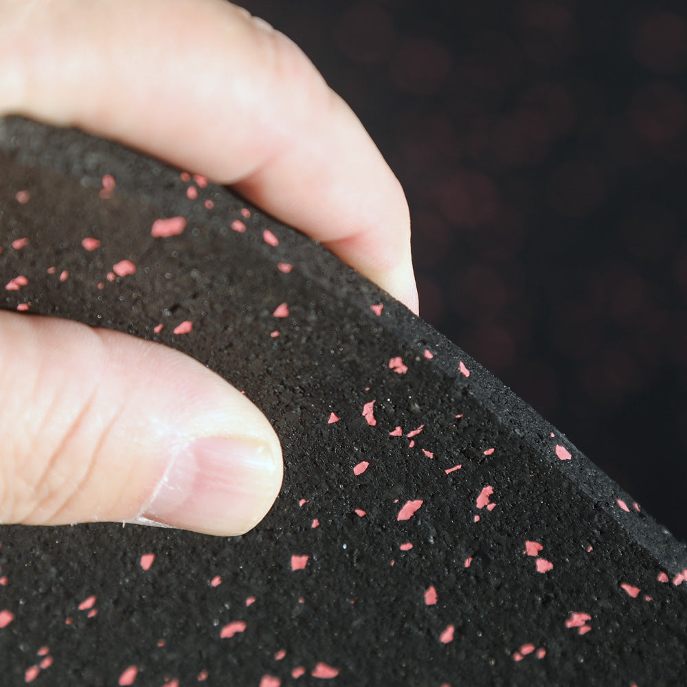 Close-up of a hand holding black rubber gym mat with red specks against a blurred background