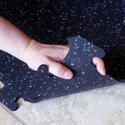 Hand holding up one corner of a 1/4" rubber gym tile over a tile floor.