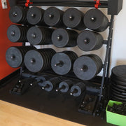 Stacked weight plates on a rack with a rubber mat under it in a gym setting.