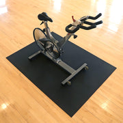 Spin bike on a black 4'x6' mat over a wooden floor.