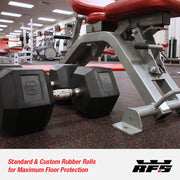 Pair of black dumbbells on a rubber roll gym floor with gym equipment in the background.