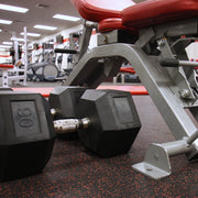 Pair of hexagonal dumbbells on a rubber roll gym floor with a weight bench in the background.