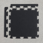 Rubber gym tile laying on a gray surface with the interlocking edge pieces laying next to the tile.