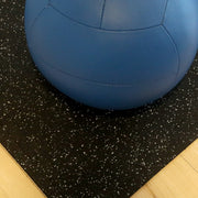 Blue exercise ball on top of gray speckled rubber gym tiles.