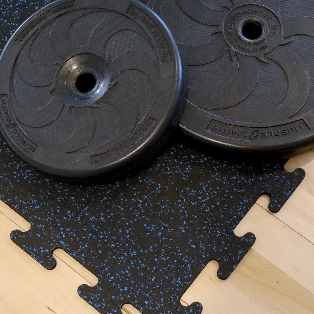 Two black weight plates on a black and blue speckled rubber gym tile.
