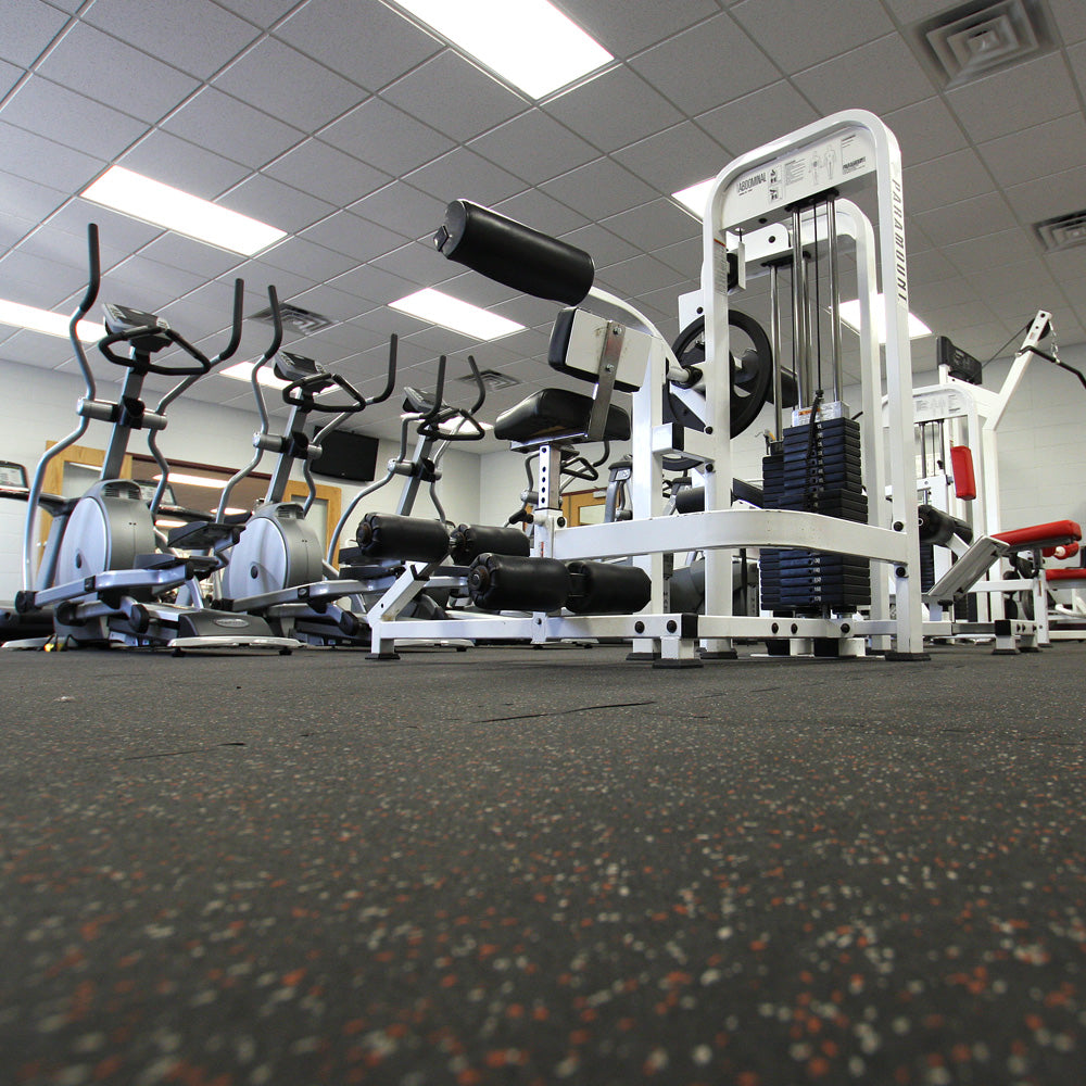 Gym interior with various exercise equipment on speckled rubber gym tiles.