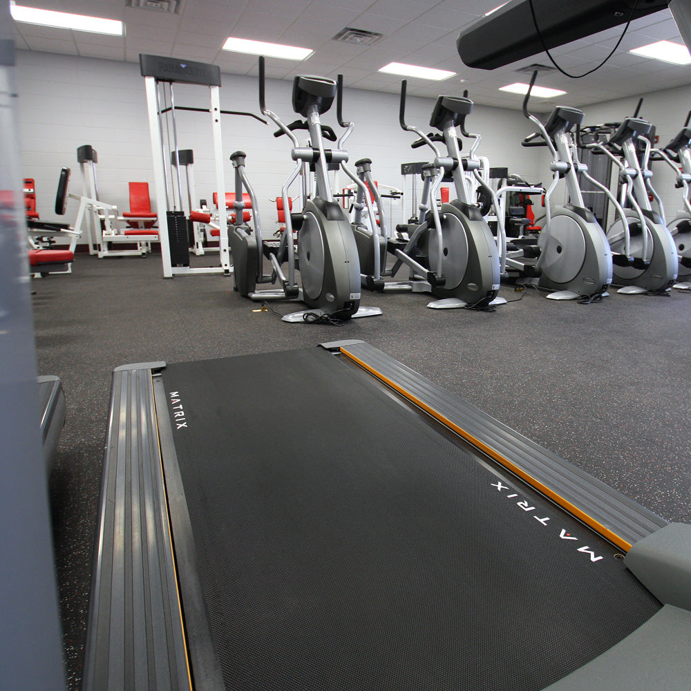 Gym interior with treadmills and stationary bikes on rubber gym tiles.