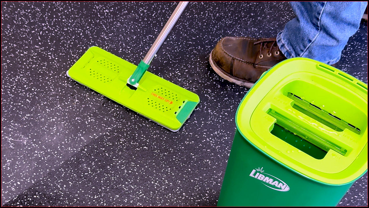 A person using a lime green microfiber mop on black rubber gym flooring.
