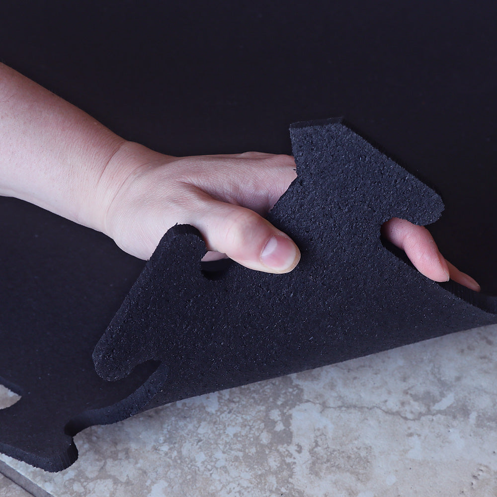 Hand holding up one corner of a 3/8" Rubber Gym Tile over a tile floor.