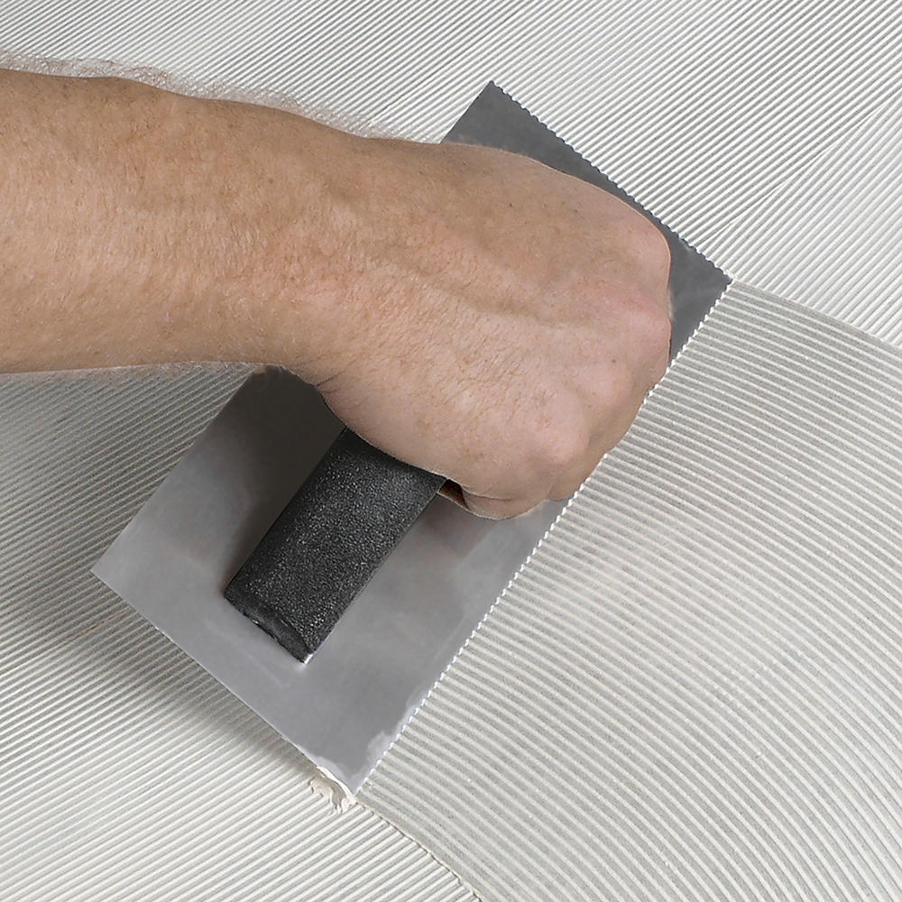 Person using v-notch trowel to spread adhesive.