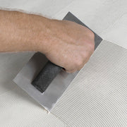 Person using v-notch trowel to spread adhesive.