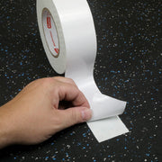 Hand peeling a strip of protection film off the back of a piece of double sided tape  on a blue speckled rubber floor.