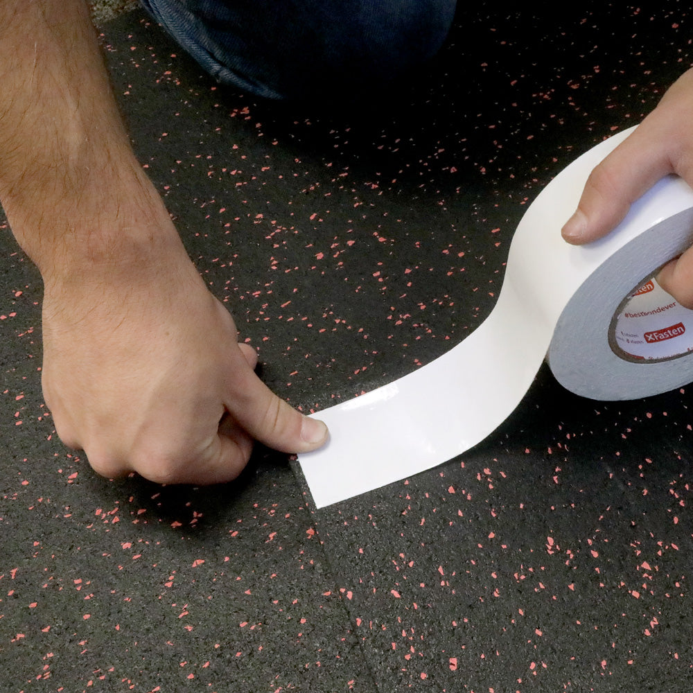 Roll of double sided tape being applied to a rubber flooring. 