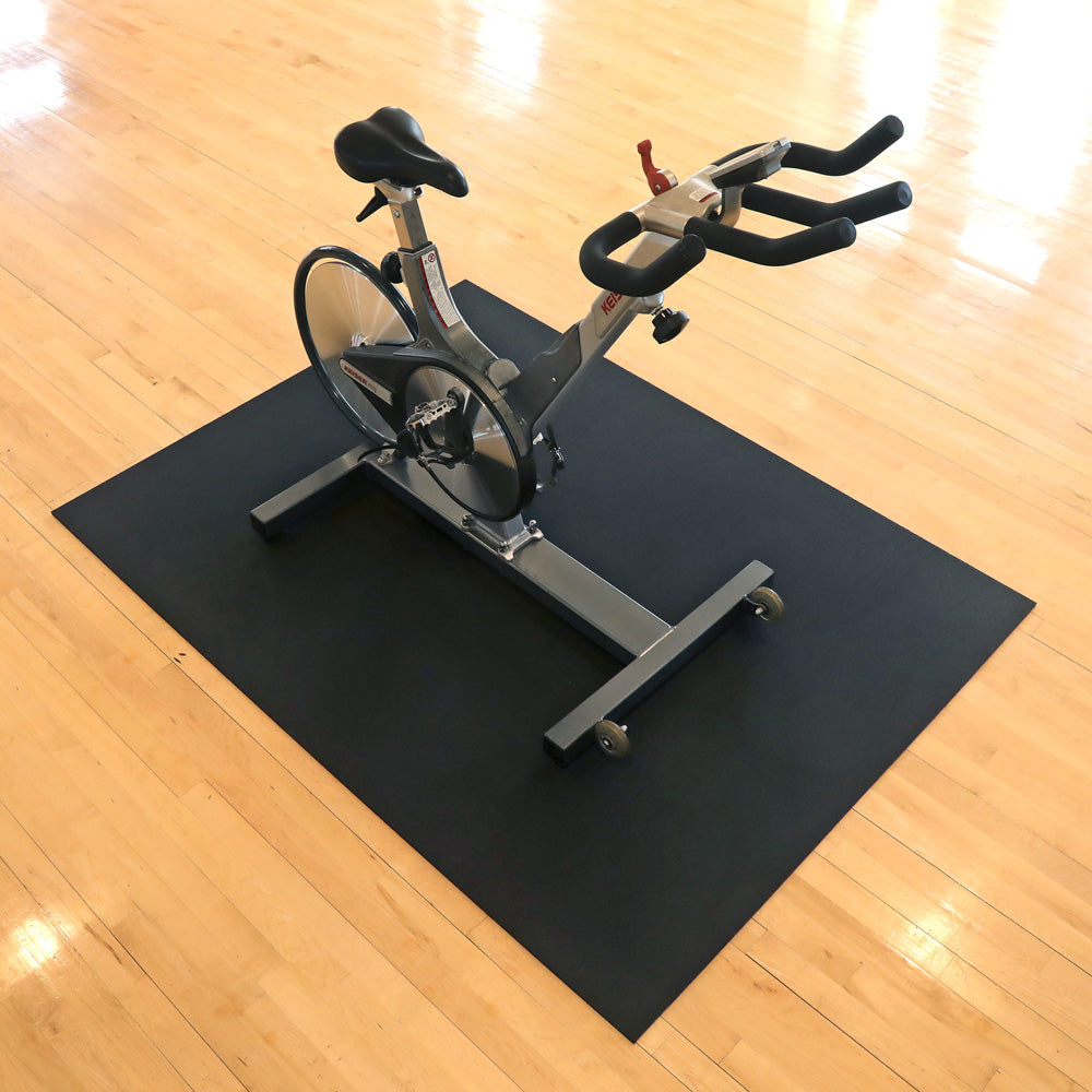 Spin bike on a black 4'x6' mat over a wooden floor.