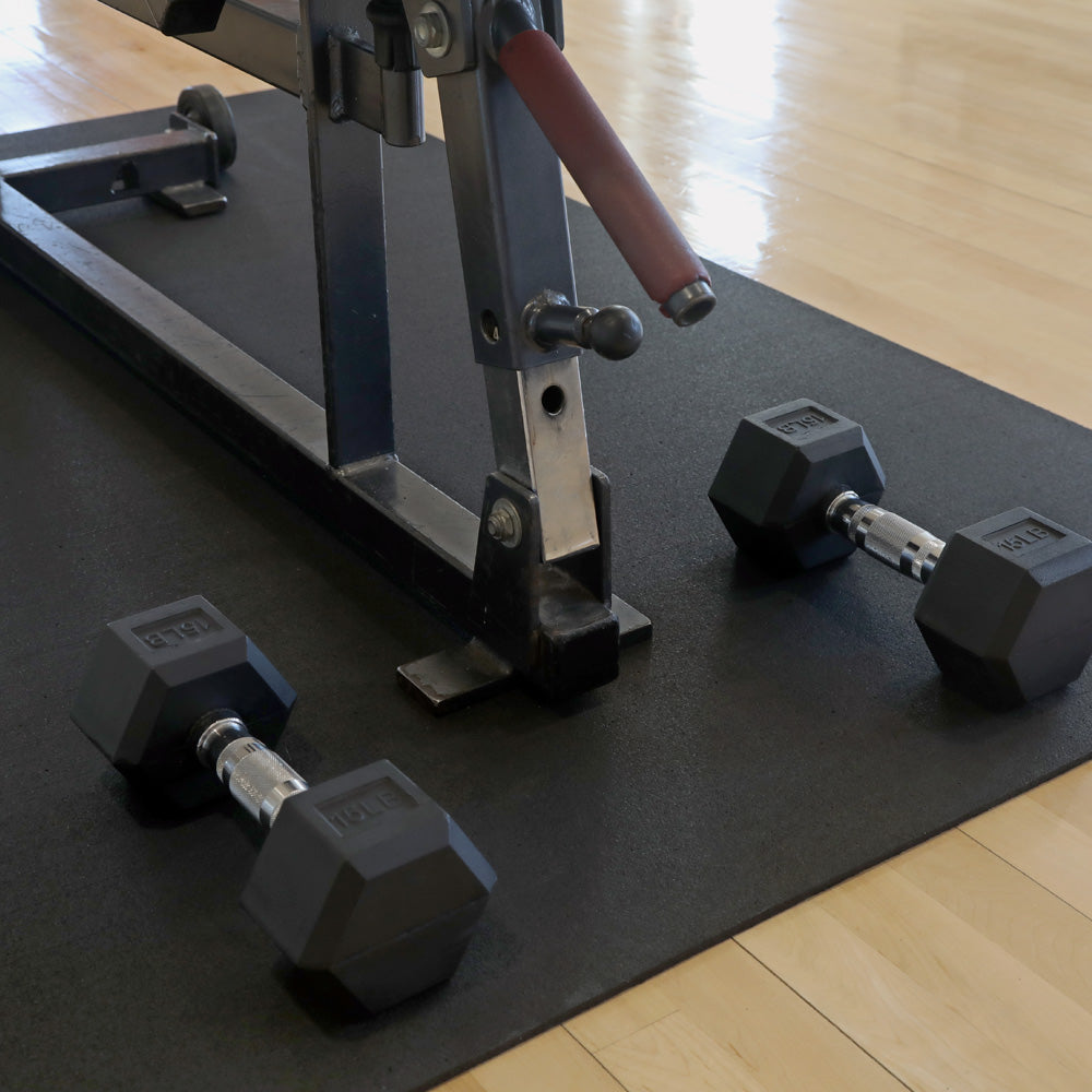 Dumbbells and a weight machine on a 4'x6' black mat in a gym setting.