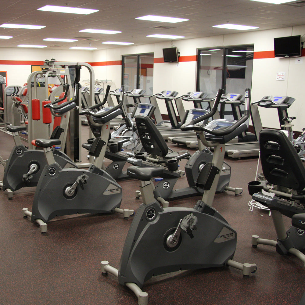 Gym interior with stationary bikes and treadmills on a terra cotta fleck rubber roll gym flooring.