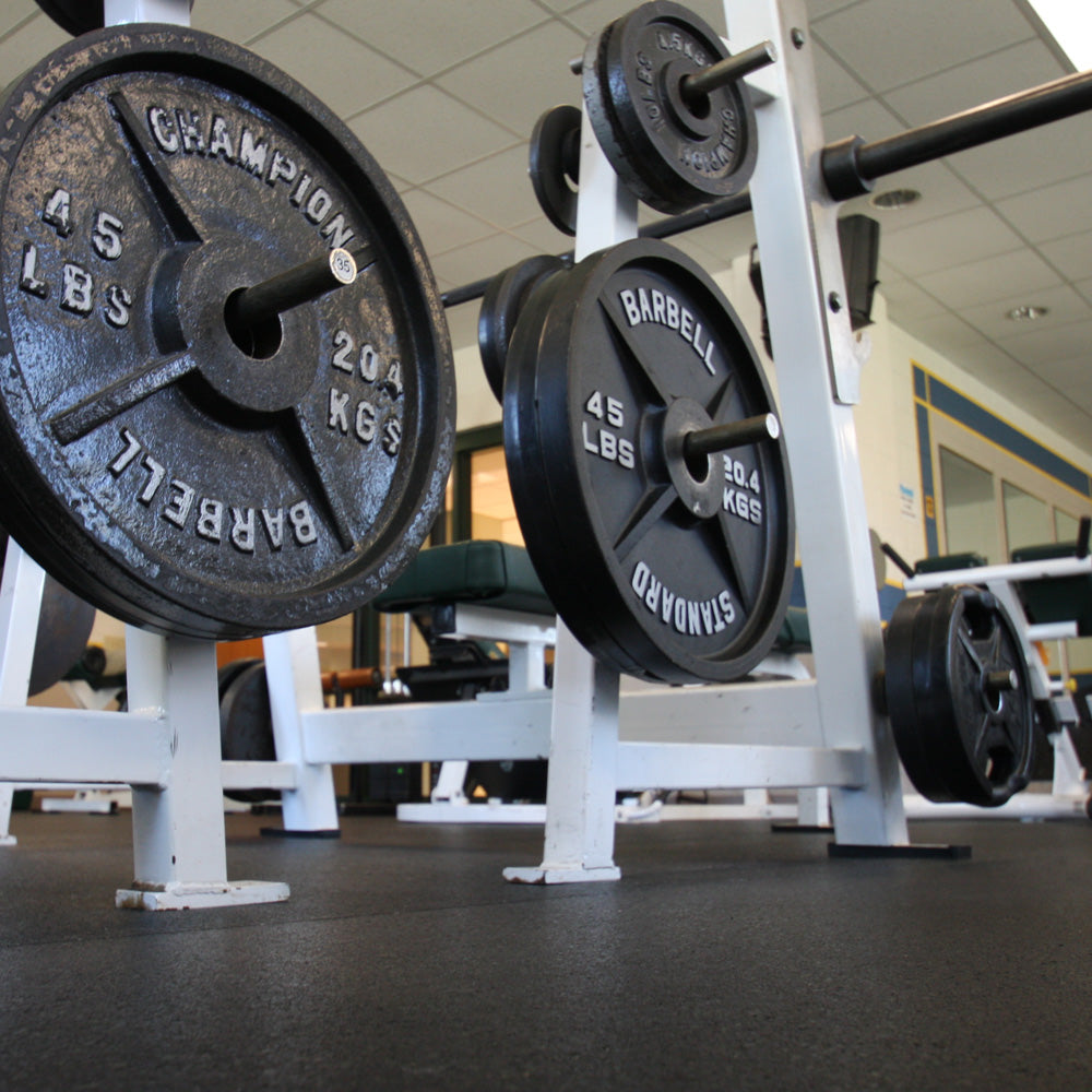 Barbell with weight plates on a rack in a gym setting over 8mm Rubber Roll flooring.