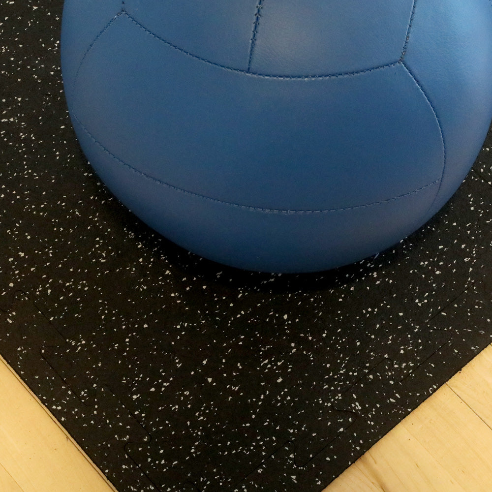 Blue exercise ball on top of gray speckled rubber gym tiles.