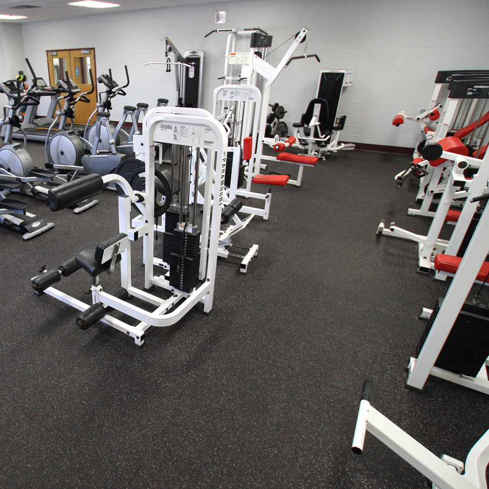 Gym interior with various exercise machines on gray fleck rubber tiles.