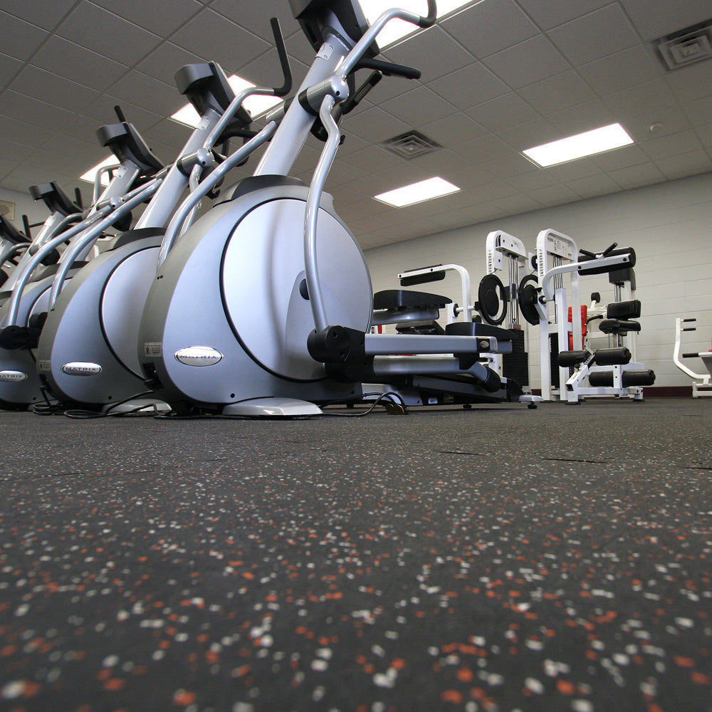 Gym interior with elliptical machines and weight racks on rubber gym tiles.