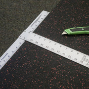 T Square laying across a roll of rubber flooring with a box cutter laying on the rubber floor next to it. 