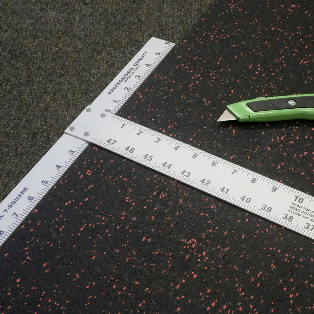 T Square laying across a roll of rubber flooring with a box cutter laying on the rubber floor next to it. 