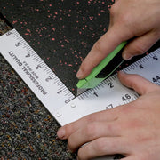 Hand using a green box cutter to score a rubber flooring roll with a T Square to keep the cut straight. 