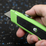 Hand holding a green utility knife with a blurred background