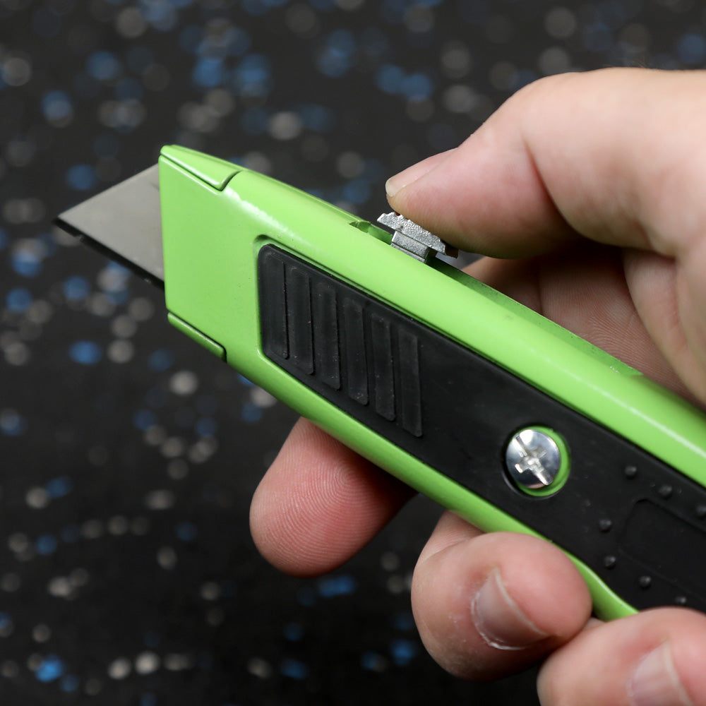 Hand holding a green utility knife with a blurred background