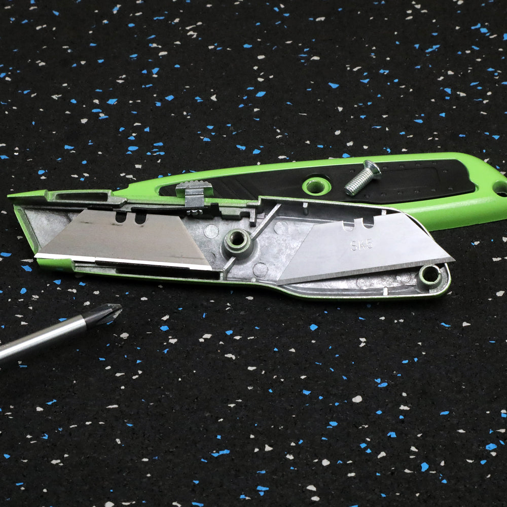 Disassembled green utility knife on a black speckled surface