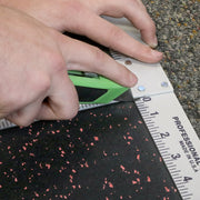 Person using a green utility knife and a T Square to cut a piece of rubber flooring. 