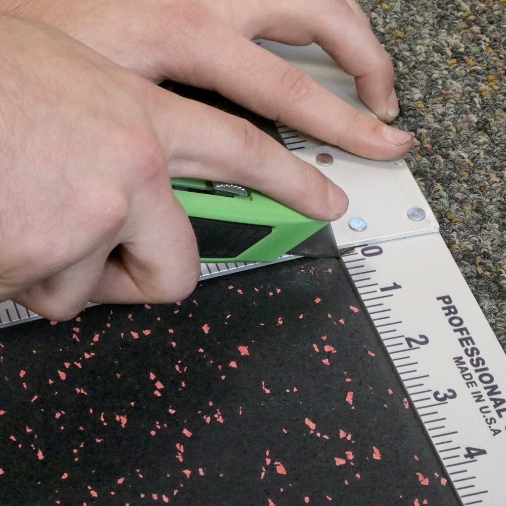 Person using a green utility knife and a T Square to cut a piece of rubber flooring. 